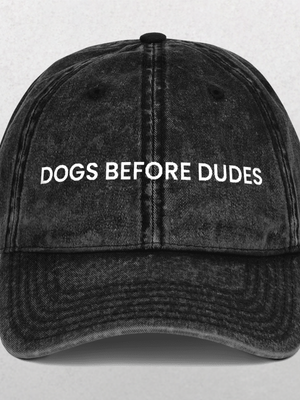 The Vintage Cap - Dogs Before Dudes is a black hat featuring the slogan DOGS BEFORE DUDES embroidered in white—an ideal, funny accessory for any dog mom.