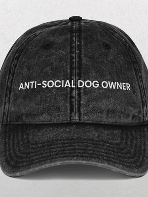 The Vintage Cap - Anti-Social Dog Owner is a black denim baseball cap with white embroidered text on the front, shown against a light gray background—an ideal slogan pet hat and fun gift for dog dads.